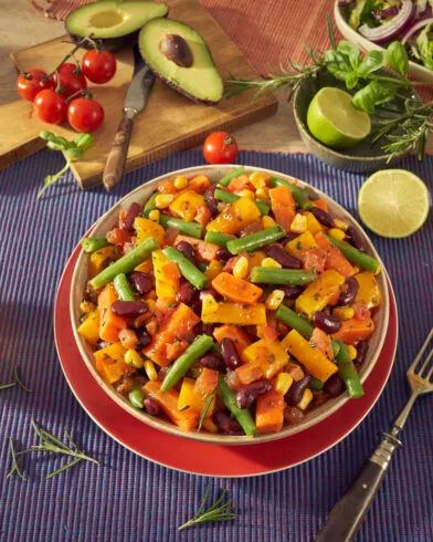 Sałatka z fasolą i mrożonymi warzywami FRoSTA Meksykańskie na patelnię w misce, otoczona awokado, limonką i tortillami.