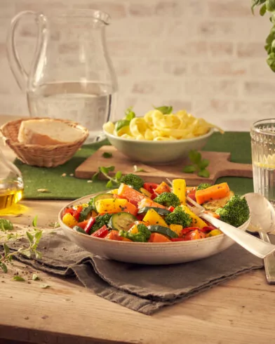 Miska sałatki, widelec, karafka i szklanka wody z cytryną, makaron, warzywa na patelnię FRoSTA, chleb, oliwa, zioła.