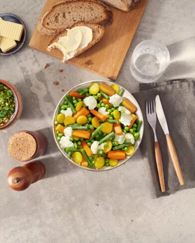 Miska komosy ryżowej z warzywami FRoSTA na stole, obok widelec, nóż, szklanka wody, chleb z masłem i sos.