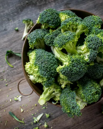 Miska z różyczkami brokułów FRoSTA na rustykalnym drewnie, obok rozsypane kawałki i łodyżki tego mrożonego produktu.