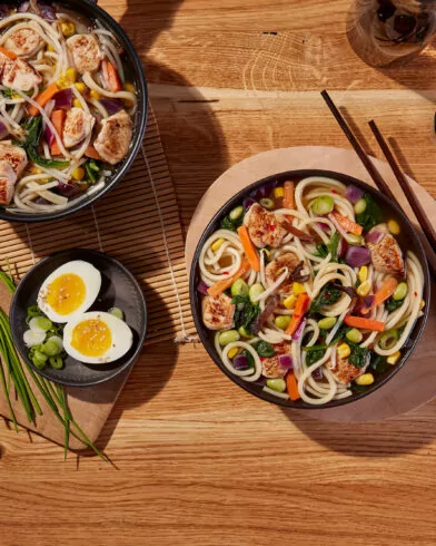 Miska ramenu z warzywami FRoSTA i kurczakiem FRoSTA, pałeczki, jajko, szczypior FRoSTA, chili, szczypiorek na stole.